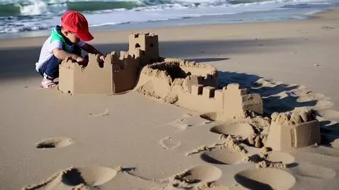 AI Video from prompt: A child in a red hat builds a sandcastle on the 