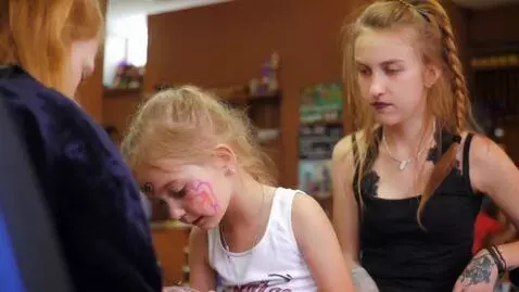 AI Video from prompt: A cute blonde girl is getting a tattoo by 2 girl