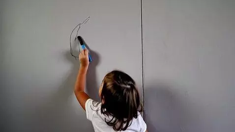 AI Video from prompt: A child in an empty room (only gray paint) draws