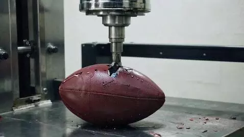 AI Video from prompt: A hydraulic press flattening a football on a met