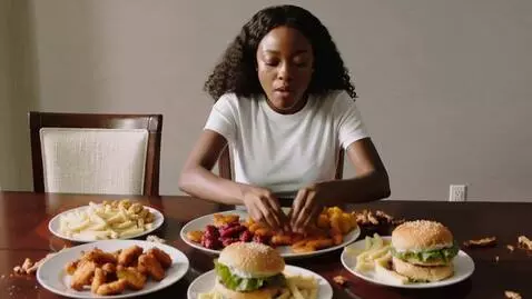 AI Video from prompt: a black woman eats a huge amount of food and bec