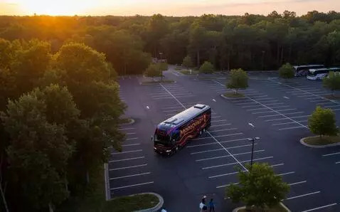 AI Video from prompt: Bus backs up to park  by other buses. Trees movi