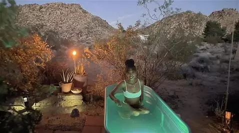 AI Video from prompt: the model steps into the outdoor bath and sits i