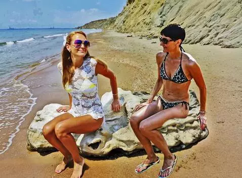AI Video from prompt: women sitting on a rock on the beach stand up, t