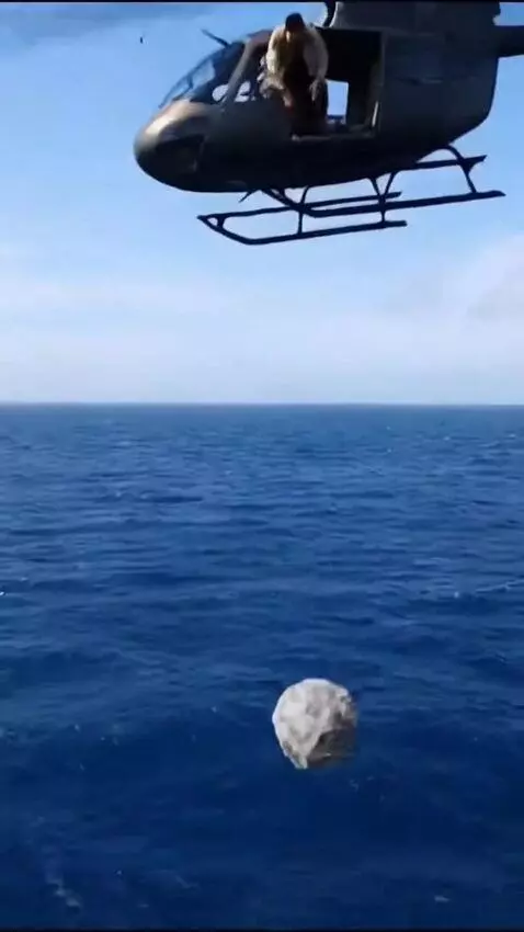 AI Video from prompt: A man in a helicopter drops a large rock into th