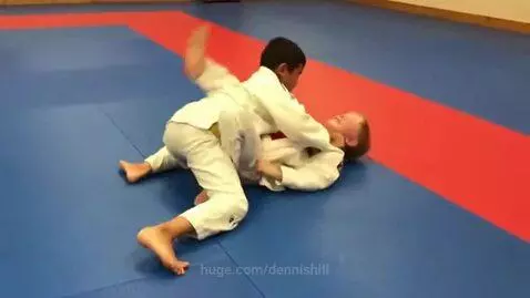 Two young boys in judo gis grappling on a mat during a ground fight training session.