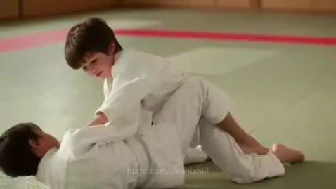 Two young boys in judo uniforms grappling on a mat during a ground fight.