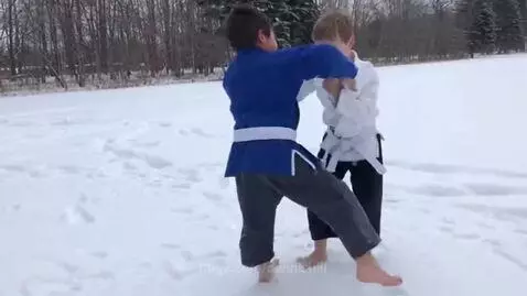 Two young boys in BJJ gis and white belts grappling in a snowy outdoor field.