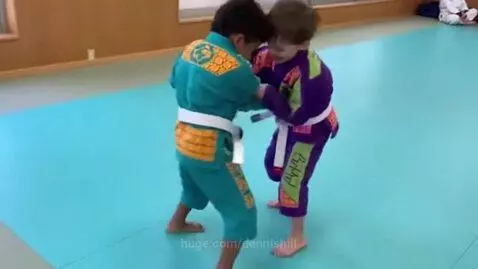 Two young boys in colorful Brazilian Jiu-Jitsu gis grappling on a blue mat, receiving instructions.