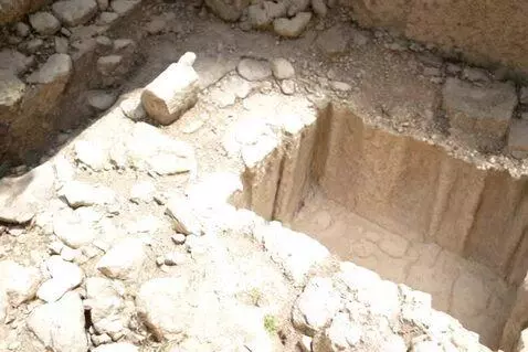 An ancient, rocky, rectangular pit resembling an empty tomb or excavation site under bright sunlight.