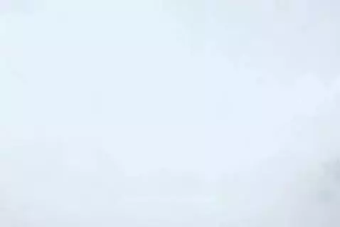 Blue sports car driving on a winding road through a lush green mountain range with a cloudy sky.