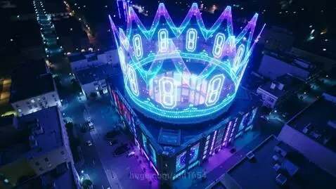 Aerial view of a futuristic neon city at night, focusing on a VR club with a large, colorful holographic crown above it.