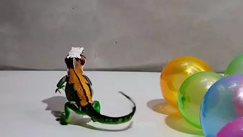 Green and orange toy lizard dancing on hind legs with colorful balloons in the background.