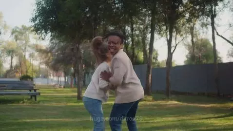 A young girl with pigtails jumps on the back of an adult woman in a grassy park.