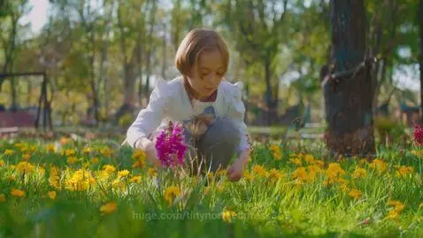 Young girl crouching in a green field with yellow flowers, picking blooms and holding a pink bouquet.