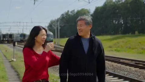 Asian couple walking outdoors by train tracks on a sunny day, smiling and interacting.