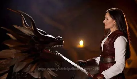 Female warrior in leather vest and gloves holds sword against a dragon's open mouth.