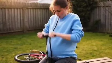 Woman outdoors using a bicycle pump, with the hose in her mouth, as her belly visibly inflates.