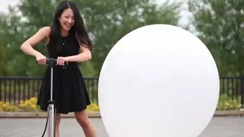 Asian woman with long dark hair in a black dress inflating a large white spherical balloon with a bicycle pump.