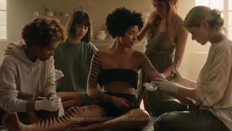 Young women applying black tribal stripes tattoo on arms and legs with brushes.