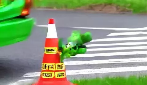 Animated green mouse with large ears jumps on a traffic cone as cars pass by on a busy road.