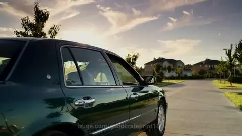 Man in white shirt closing car door and driving away in a dark green sedan at sunset.