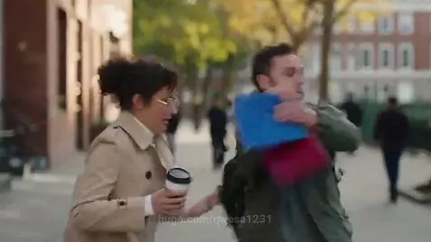 Man in green jacket playfully steals a book from a woman in a beige coat on a city street, who then chases him.