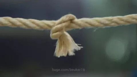 Close-up of a thick, light-colored rope with a knot in the center, showing frayed ends and texture.