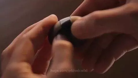 Close-up of hands slowly applying pressure to a dark spherical object until it cracks open.