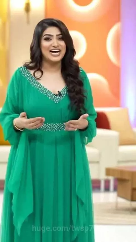 Plus-size Pakistani model in an emerald green dress telling a joke in a bright studio.