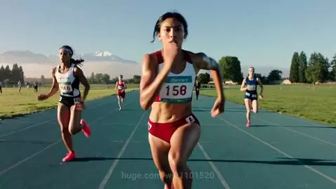 Female athletes in a competitive race on a blue running track with mountains in the background.