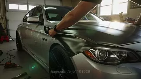Silver BMW sedan being modified with matte black vinyl wrap and illuminated by blue LED lights.