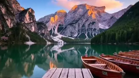 Tranquil mountain lake with snow-capped peaks reflecting in emerald water at sunrise or sunset.