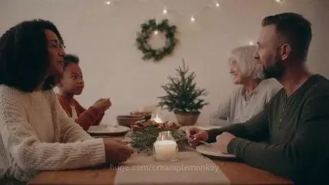 Diverse family of four smiling around a warmly lit Christmas dinner table with decorations.