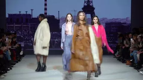 Models walk down an expressway runway in Paris fashion show with industrial backdrop and excited audience.