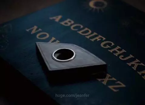 Close-up of a dark Ouija board with a triangular planchette moving across alphabet letters.