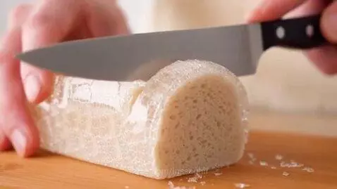 Close-up of a knife cutting a translucent, crystalline bread loaf, revealing its texture and creating small, clear pieces.