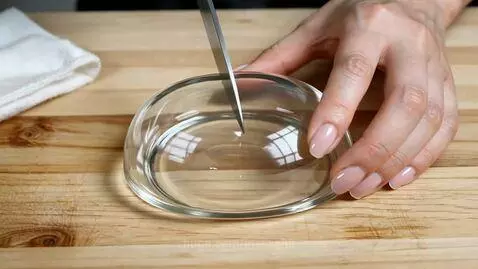 Hands slicing a clear, dome-shaped object resembling glass bread on a wooden board, showing a spiral pattern inside.