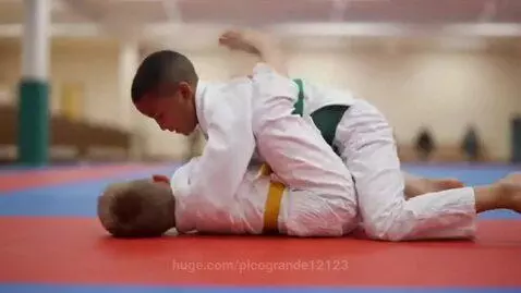 Two young boys in judo uniforms practicing ground fighting and grappling on a mat.