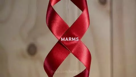 Close-up of a red satin ribbon twisted into a figure-eight shape with 'MARMS' text on a blurred wooden background.