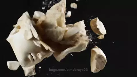 Slow motion video of an ancient Greek marble statue head shattering into many fragments against a black background.
