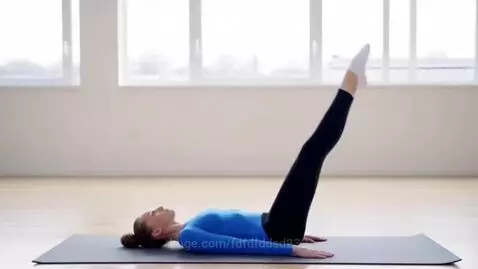 Gymnast lying on back, lowering legs into a perfect middle split on a yoga mat.