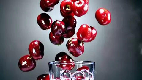 Ultra-realistic macro shot of frozen red cherries falling into a glass with ice cubes, creating juice splashes.