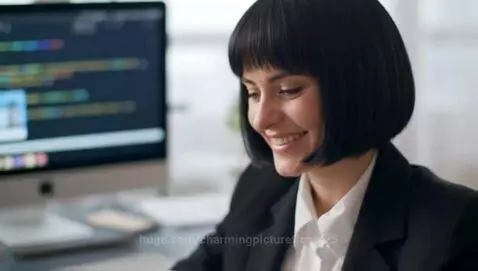 Professional Russian woman with bob haircut in business suit at desk, smiling, with web development visuals on screen.