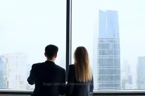Couple in business suits looking out a large window at a city skyline with skyscrapers.