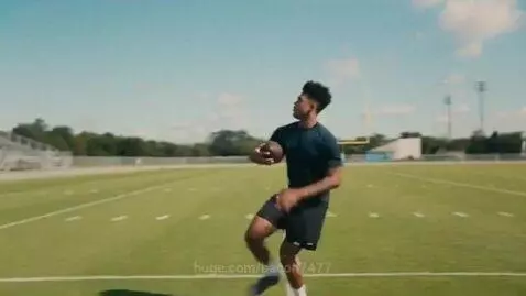 Young man in dark t-shirt and shorts running and catching a football on a green field.