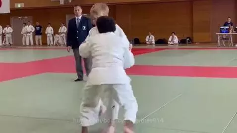 Two boys in white judo uniforms competing in a match, one performing a hip throw.