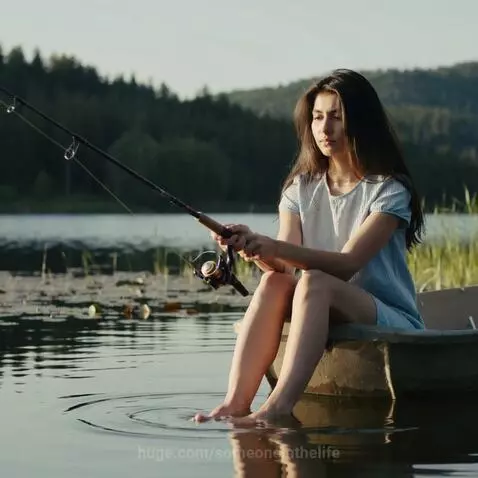 Young woman with long dark hair fishing from a boat, her bare feet in the calm lake water.