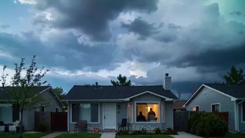 Time-lapse of fast-moving clouds over residential houses, zooming into an apartment window with silhouettes inside.