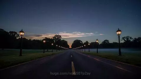 A straight park road transitioning from a hazy night with lanterns to a bright morning with sunrise illuminating trees and dew-kissed grass.